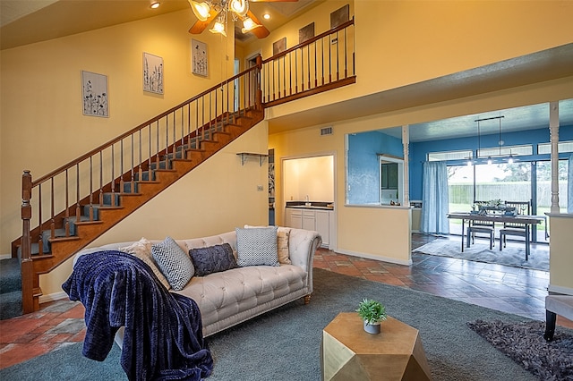 living room featuring stone tile floors, a towering ceiling, ceiling fan, baseboards, and stairs