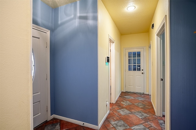 hall with a textured ceiling, stone tile flooring, and baseboards