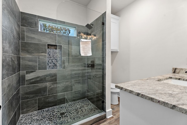 full bathroom with toilet, a tile shower, wood finished floors, and vanity