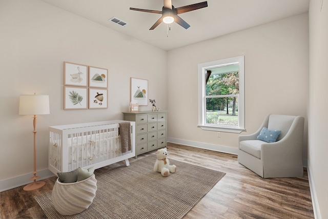 bedroom with light wood finished floors, visible vents, ceiling fan, a crib, and baseboards