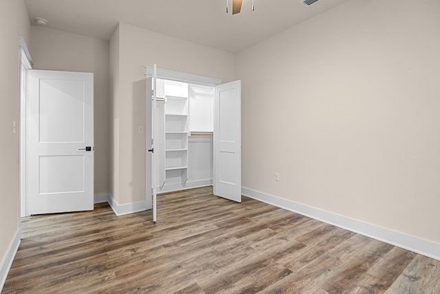 unfurnished bedroom with baseboards, a ceiling fan, wood finished floors, a spacious closet, and a closet