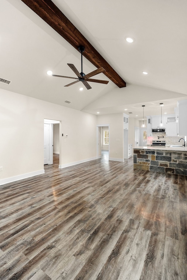 unfurnished living room with baseboards, visible vents, lofted ceiling with beams, dark wood-type flooring, and a sink