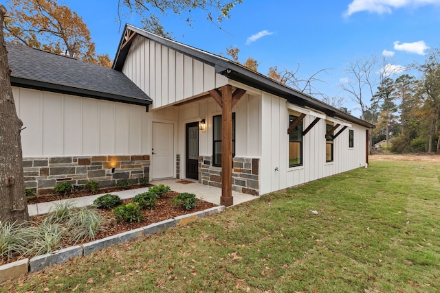 view of home's exterior featuring stone siding, a lawn, board and batten siding, and roof with shingles