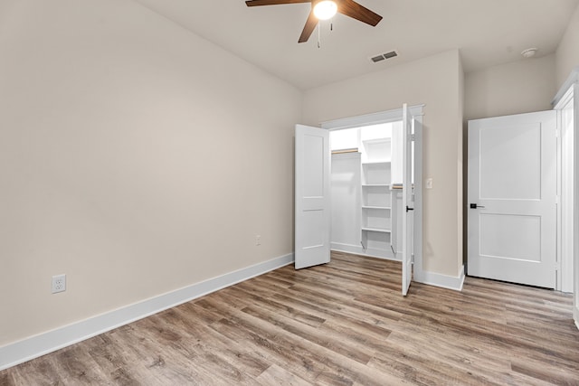 unfurnished bedroom with a walk in closet, visible vents, light wood-style flooring, ceiling fan, and baseboards