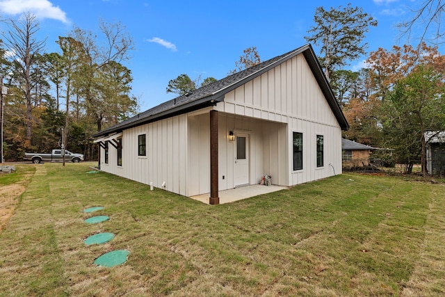 rear view of property with board and batten siding, a lawn, and a patio