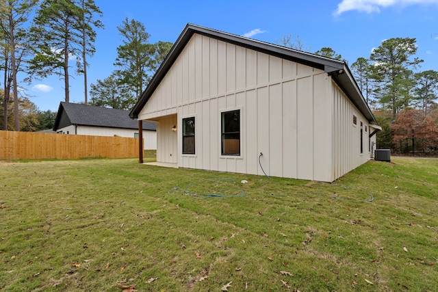 back of property featuring board and batten siding, fence, central AC unit, and a lawn