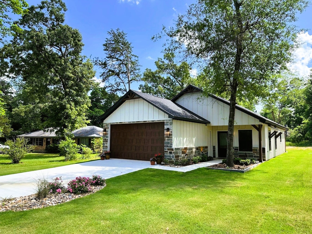 view of front facade with a front lawn, stone siding, concrete driveway, an attached garage, and board and batten siding