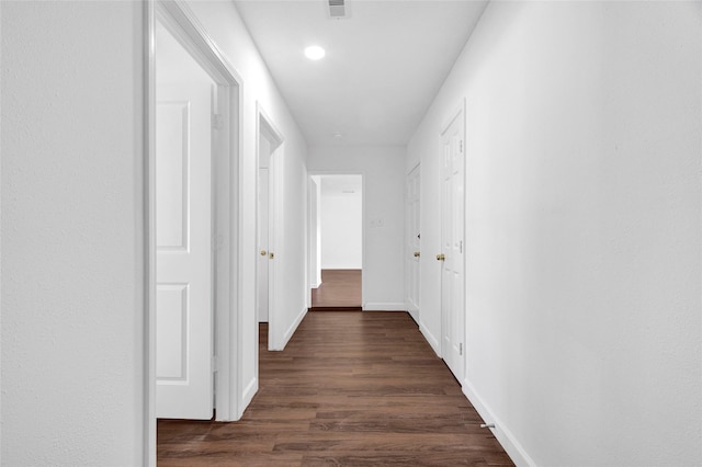 hallway with visible vents, baseboards, and dark wood-style flooring