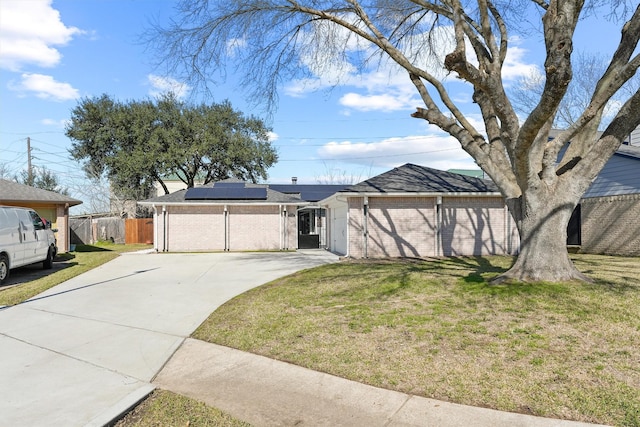 view of front facade with solar panels, brick siding, fence, concrete driveway, and a front lawn