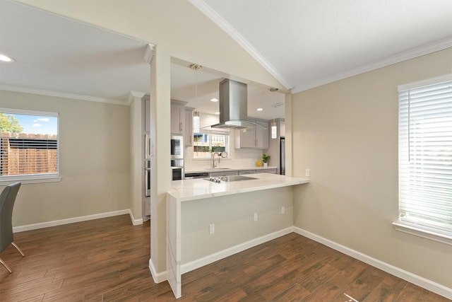 kitchen with light countertops, hanging light fixtures, a sink, island range hood, and a peninsula