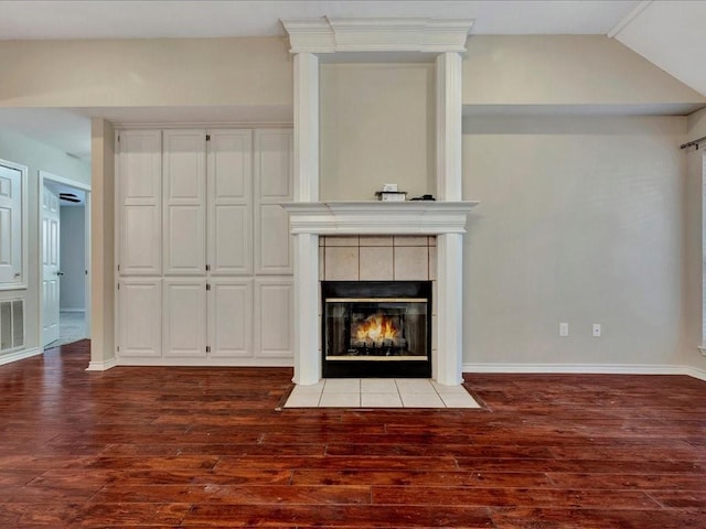 unfurnished living room with dark wood-type flooring, a tile fireplace, visible vents, and baseboards