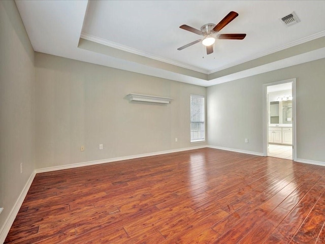 empty room featuring hardwood / wood-style flooring, a ceiling fan, baseboards, ornamental molding, and a raised ceiling