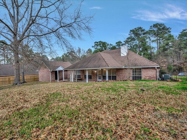 back of house featuring brick siding, a chimney, fence, and a yard