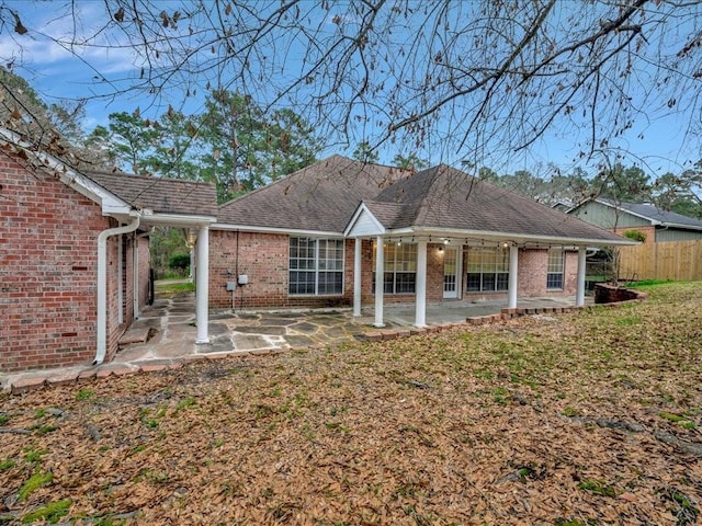 rear view of house with a shingled roof, a patio area, brick siding, and a lawn