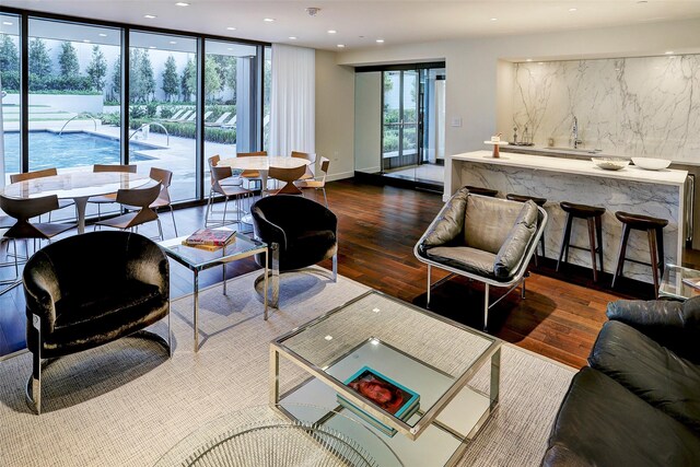 living room featuring wood finished floors, baseboards, recessed lighting, indoor wet bar, and floor to ceiling windows