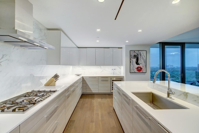 kitchen with light wood-type flooring, stainless steel gas stovetop, modern cabinets, wall chimney exhaust hood, and a sink