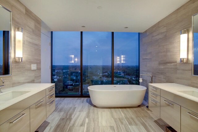 full bath with a sink, a freestanding tub, two vanities, and tile walls