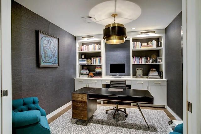 home office with baseboards, built in shelves, an accent wall, and wallpapered walls