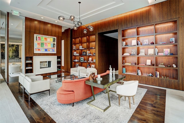 living area with built in features, wood walls, and a tray ceiling