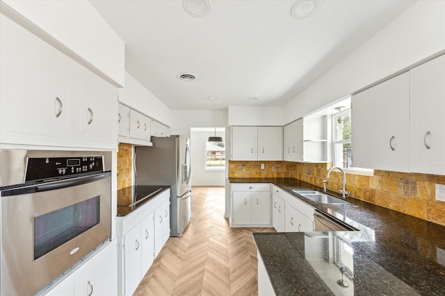 kitchen featuring white cabinets, decorative backsplash, dark countertops, stainless steel appliances, and a sink