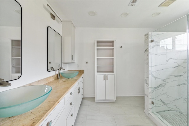 full bath featuring double vanity, a marble finish shower, visible vents, and a sink