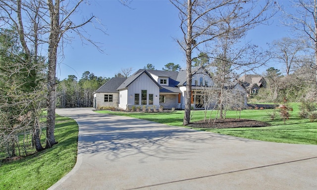 view of front of house featuring roof with shingles, concrete driveway, board and batten siding, a front yard, and stone siding