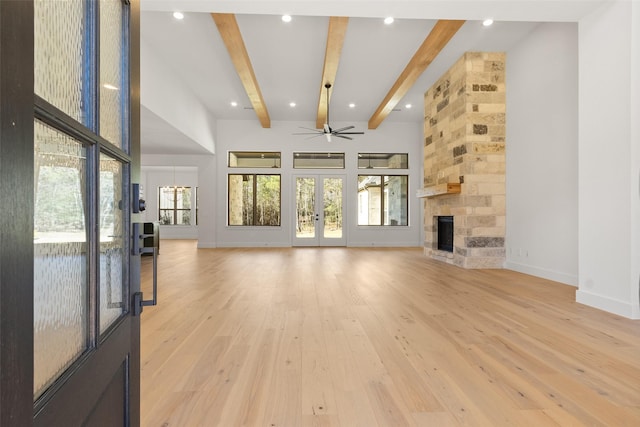 unfurnished living room with light wood-style floors, a wealth of natural light, a large fireplace, and beam ceiling