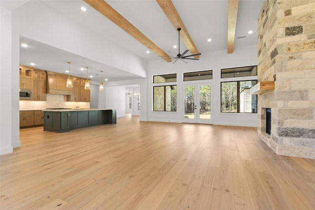 unfurnished living room with light wood finished floors, baseboards, beamed ceiling, a stone fireplace, and french doors