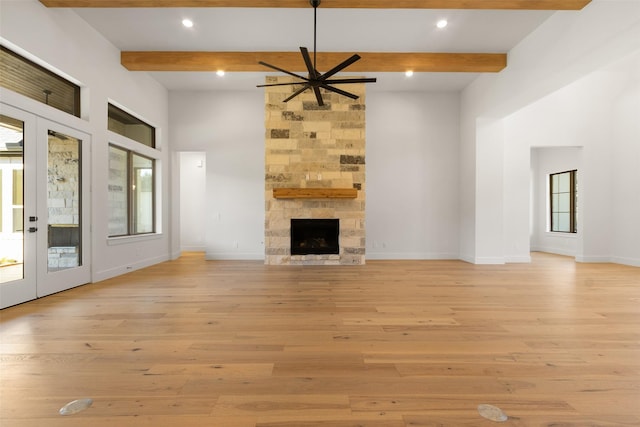 unfurnished living room with light wood finished floors, french doors, a stone fireplace, and beamed ceiling