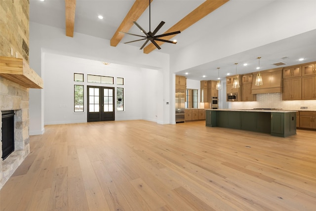 unfurnished living room featuring french doors, beam ceiling, a towering ceiling, a stone fireplace, and light wood-type flooring