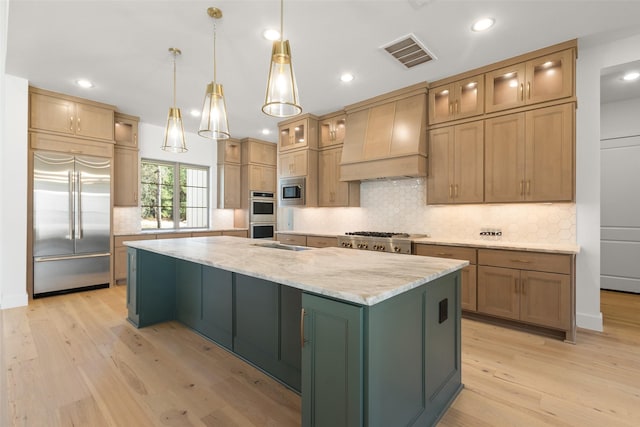 kitchen featuring built in appliances, premium range hood, a spacious island, visible vents, and light wood-type flooring