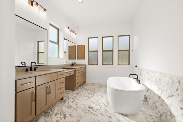 full bathroom featuring marble finish floor, two vanities, a sink, and a soaking tub