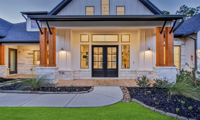 view of exterior entry featuring stone siding, roof with shingles, board and batten siding, and french doors