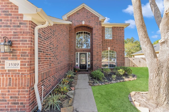 view of exterior entry featuring fence, a lawn, and brick siding