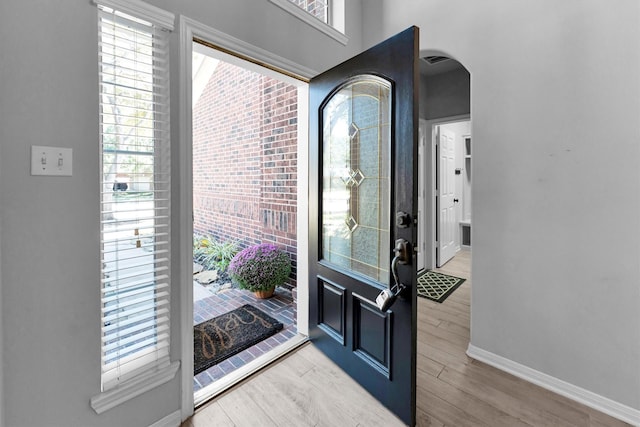 entryway with light wood-style flooring, baseboards, and arched walkways