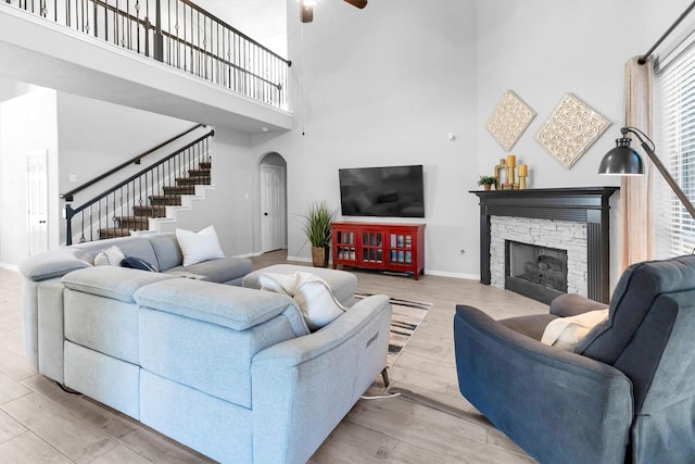 living area with light wood finished floors, baseboards, arched walkways, stairway, and a stone fireplace