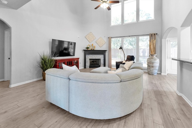 living room with arched walkways, a stone fireplace, light wood-type flooring, and baseboards