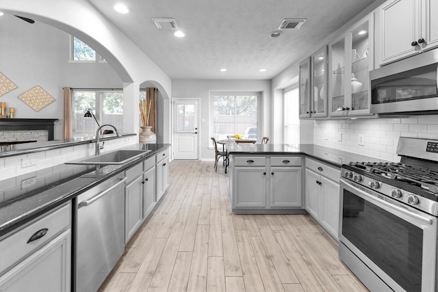 kitchen featuring dark countertops, appliances with stainless steel finishes, glass insert cabinets, and a sink