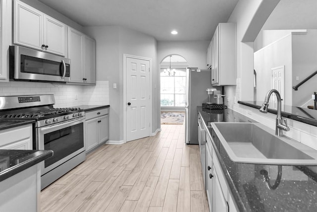 kitchen with arched walkways, tasteful backsplash, appliances with stainless steel finishes, white cabinetry, and a sink