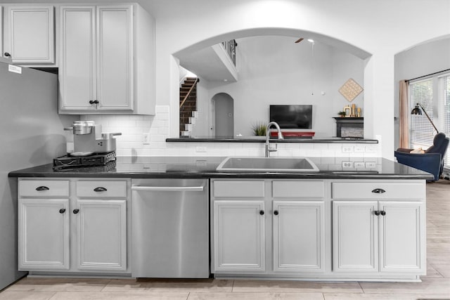 kitchen featuring tasteful backsplash, dark countertops, white cabinets, a sink, and dishwasher