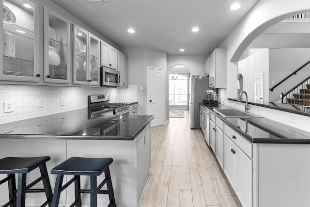 kitchen with arched walkways, a peninsula, white cabinets, appliances with stainless steel finishes, and glass insert cabinets