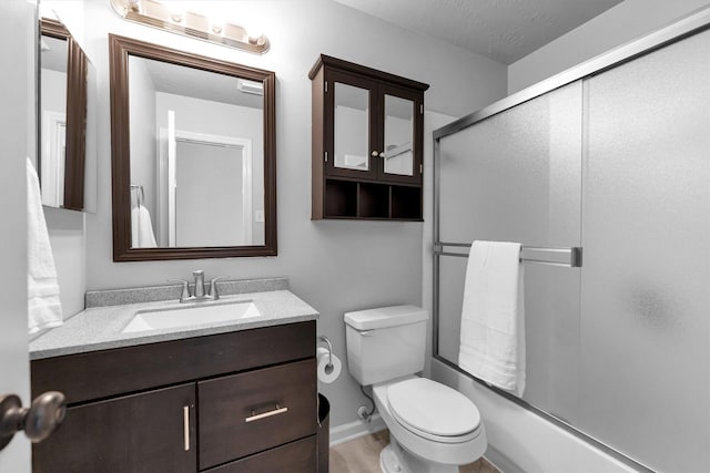 full bathroom featuring baseboards, vanity, toilet, and bath / shower combo with glass door