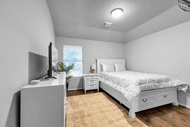 bedroom featuring baseboards, visible vents, lofted ceiling, dark wood-type flooring, and a textured ceiling