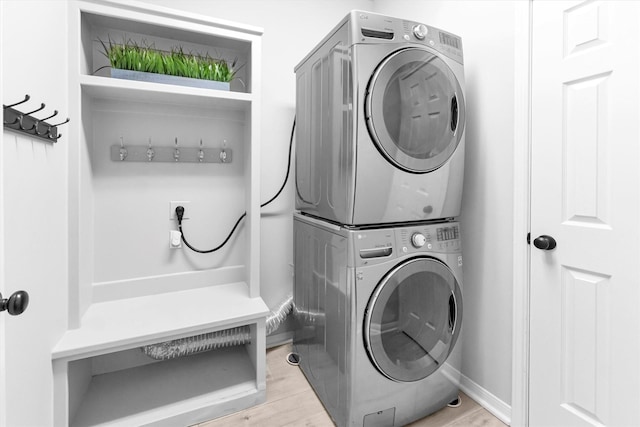 laundry area featuring laundry area, stacked washing maching and dryer, light wood-style flooring, and baseboards