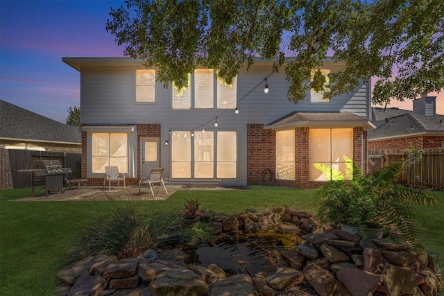 back of property featuring a patio, brick siding, a lawn, and fence