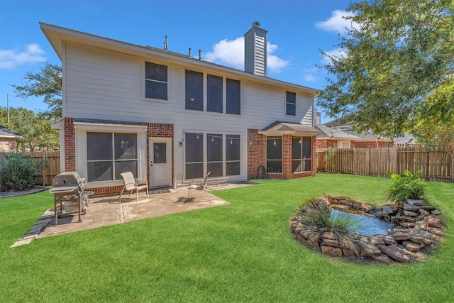 back of house with a chimney, brick siding, a lawn, and a fenced backyard