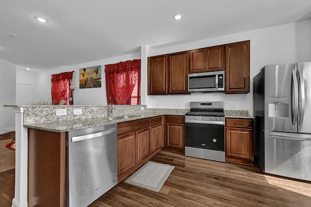 kitchen featuring appliances with stainless steel finishes, dark wood-type flooring, a sink, and a peninsula