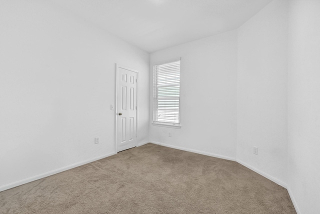 spare room with baseboards and light colored carpet