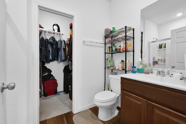 bathroom with toilet, wood finished floors, vanity, a stall shower, and a walk in closet