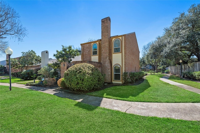 view of side of home with brick siding, a lawn, a chimney, and fence